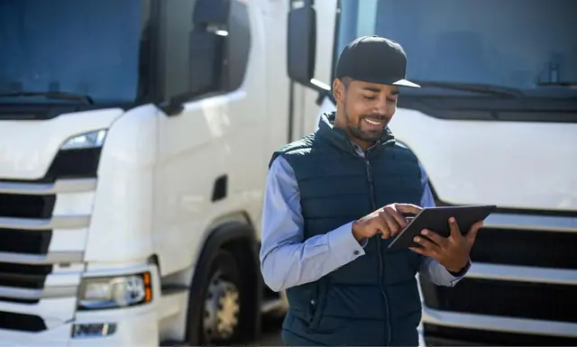 A driver holding a phone beside a truck in a yard